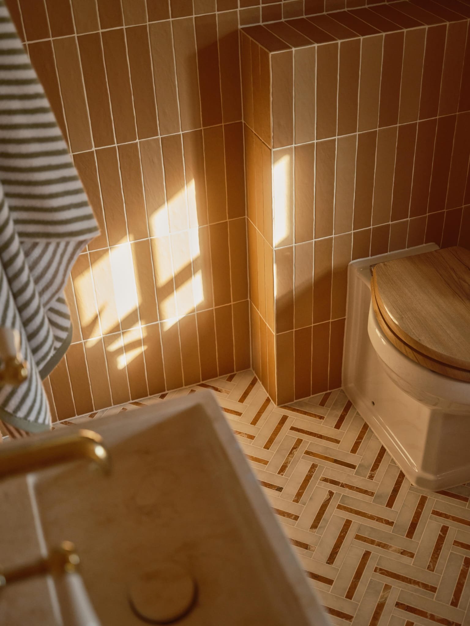 Luxury bathroom with herringbone floor tiling and brass fittings by Lucian Bathrooms in North London