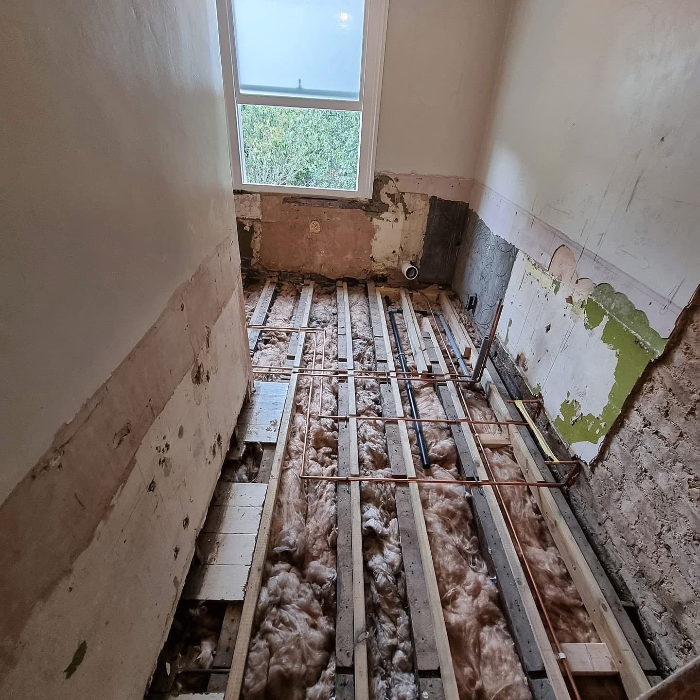 Bathroom first fix with copper pipework run between reinforced floor joists in a North London renovation