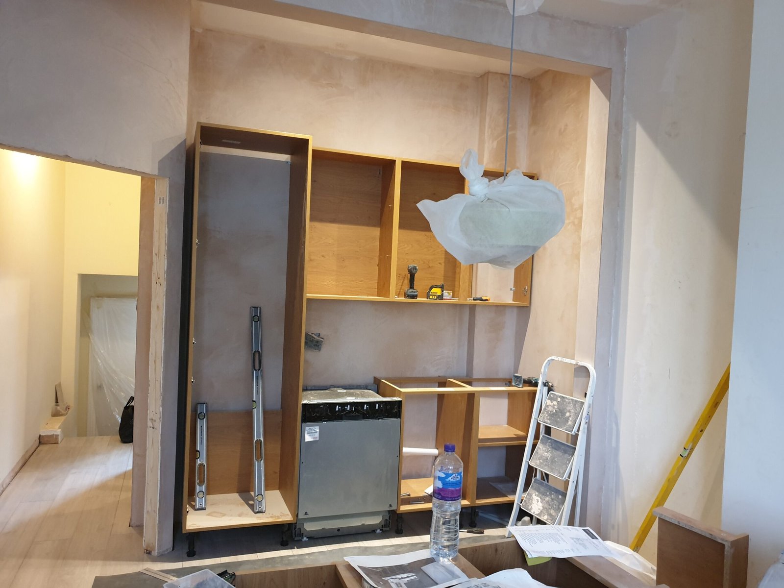 Kitchen cabinet installation with integrated dishwasher and spirit level alignment on a freshly plastered wall in North London